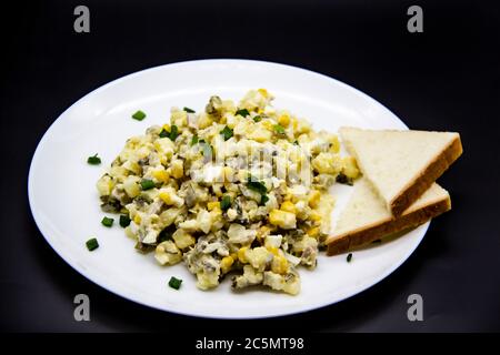 Insalata Ucraina e russa Olivier secondo una nuova ricetta su un piatto bianco. Insalata sana Olivier con carne, mais e fette di pane bianco. DELIC Foto Stock