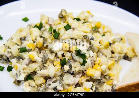 Insalata Ucraina e russa Olivier secondo una nuova ricetta su un piatto bianco. Insalata sana Olivier con carne, mais e fette di pane bianco. DELIC Foto Stock