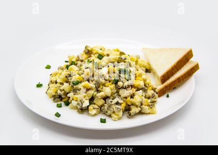 Insalata Ucraina e russa Olivier secondo una nuova ricetta su un piatto bianco. Insalata sana Olivier con carne, mais e fette di pane bianco. DELIC Foto Stock