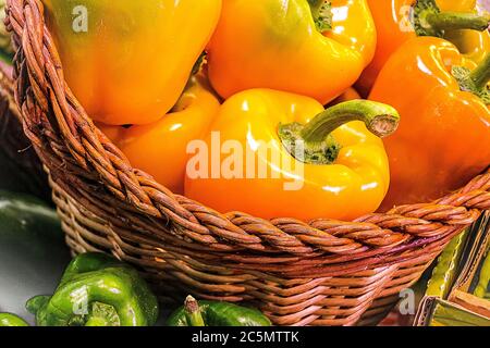 Peperoni freschi di colore arancione e giallo in cestino rosso Foto Stock