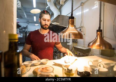 Chef che lavora all'interno della cucina, finendo un piatto per il servizio di un ristorante moderno. Foto Stock