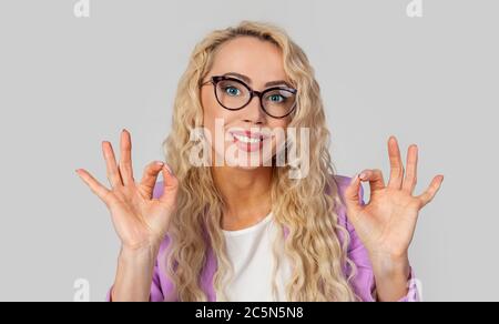 Ritratto di una felice donna positiva e carismatica in occhiali, che mostra segni ok e sorridente in approvazione, raccomando. Donna che fa doppio rubinetto. OK. Foto Stock