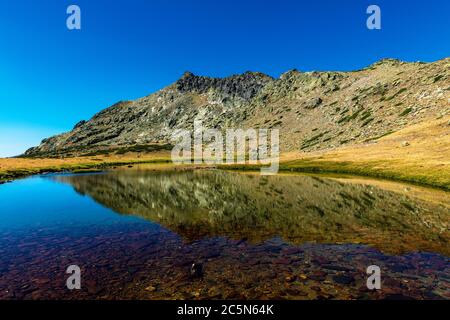 La vetta del Peñalara si riflette su un lago glaciale, la vetta più alta della catena montuosa del Guadarrama nella catena montuosa spagnola sistema Central. Foto Stock