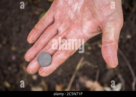 Un digger maschile ha trovato una vecchia moneta storica nella foresta e la lava Foto Stock