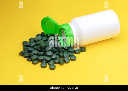 Primo piano compresse di spirulina alghe. Compresse di clorella isolate su sfondo giallo. Dieta e nutrizione, superfood vegan biologico stile di vita sano conce Foto Stock