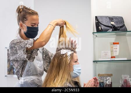 Parrucchiere indossando maschera mentre lavora e tagliando i capelli in parrucchiere come il coronavirus lockdown eases in Inghilterra 4 luglio 2020 Foto Stock