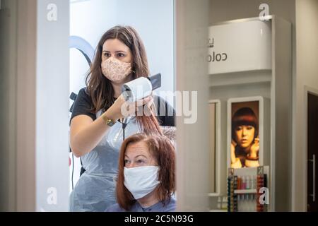 Parrucchiere indossando maschera mentre lavora e tagliando i capelli in parrucchiere come il coronavirus lockdown eases in Inghilterra 4 luglio 2020 Foto Stock