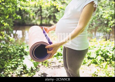 Donna giovane incinta irriconoscibile che si prepara a fare yoga con tappetino rosa yoga. Futuro attivo sport madre stile di vita. Gravidanza sana Foto Stock
