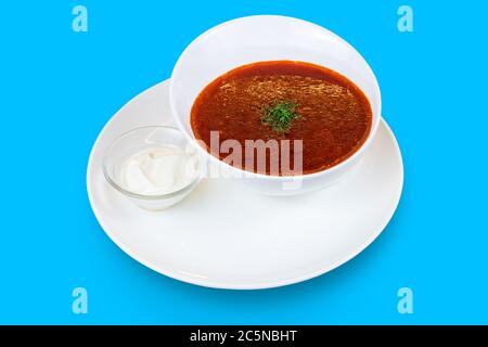 Una ciotola di borscht guarnita con aneto e panna acida isolato su sfondo blu Foto Stock