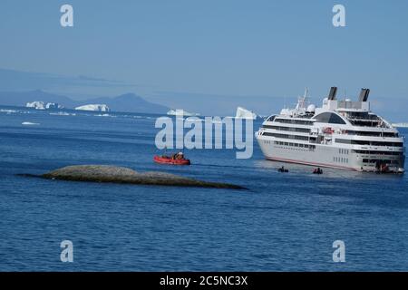 Il piccolo peschereccio da pesca rosso si alza a bordo dei passeggeri delle navi da crociera per la loro indimenticabile navigazione intorno a giganteschi iceberg. Foto Stock