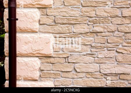 muro di un edificio pavimentato con pietra decorativa e tubo tempesta. Foto Stock