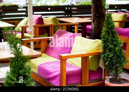 sedie morbide con cuscini in tessuto di colore verde e rosa al tavolo di legno del caffè estivo. Foto Stock