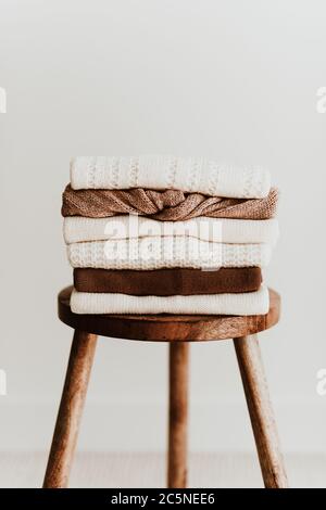 Composizione moda donna. Caldo inverno donna vollen maglia pullover impilare su uno sgabello di legno su sfondo bianco. Concetto di abbigliamento moderno Foto Stock