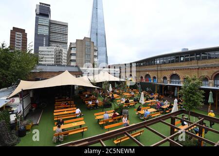 La gente gusteranno bevande al bar Acetar Yard, Londra, riaprirsi dopo l'allentamento delle restrizioni di blocco del coronavirus in tutta l'Inghilterra. Foto Stock