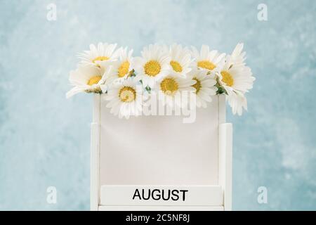 Calendario cubo bianco per agosto decorato con fiori margherita su blu con spazio copia Foto Stock