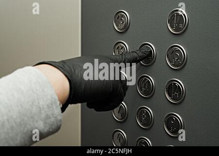 Premendo i pulsanti nell'ascensore con guanti, gomito. Quarantena e sicurezza pandemica. Foto Stock