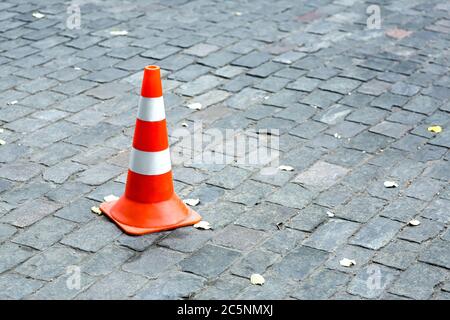 cono stradale arancione con strisce bianche si erge sulla carreggiata delle pietre da pavimentazione con spazio per la copia del testo. Foto Stock