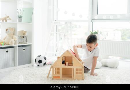 Simpatico ragazzo che gioca da solo con casa di legno nella stanza dei bambini Foto Stock