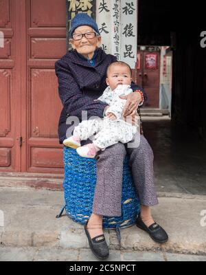 Vecchia nonna cinese seduta giù e tenendo la nipote del bambino nella sua città natale Dali, Cina del sud-ovest. Foto Stock