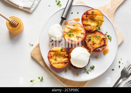 Pesche grigliate con Thyme, Miele e scoop di gelato alla vaniglia su piatto bianco, vista dall'alto, spazio per fotocopie. pesche arrosto o nettarine fatte in casa al barbecue, rus Foto Stock