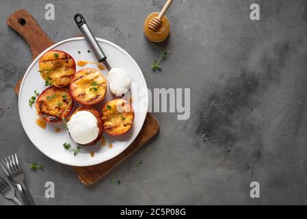 Pesche grigliate con Thyme, Miele e scoop di gelato alla vaniglia su fondo di cemento, vista dall'alto, spazio per la copia. pesche arrosto o nettari al barbecue fatti in casa Foto Stock