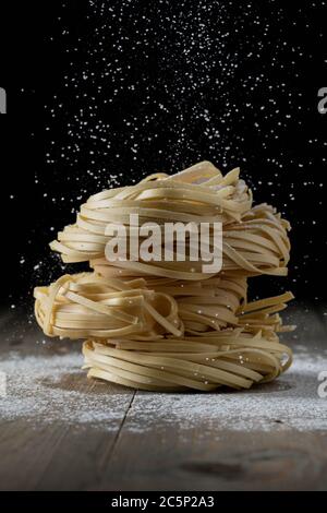 tagliatelle grezze di uova accatastate su legno e farina che cade Foto Stock