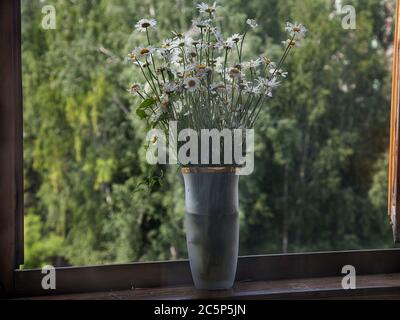 Un grande e bel bouquet di margherite in un vaso di vetro si erge su una finestra aperta in una giornata estiva. Natura. Fiori. Foto Stock