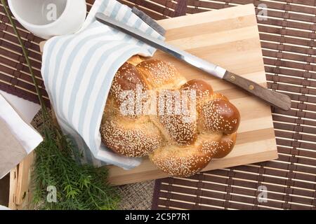 un filone intrecciato di pane all'uovo di sesamo su un legno tagliere con coltello isolato su bianco Foto Stock