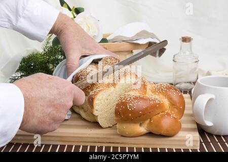 un panettiere taglia una fetta di un filone intrecciato di pane all'uovo di sesamo su un tagliere di legno Foto Stock