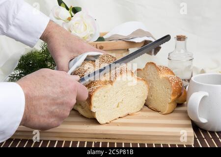 un panettiere taglia una fetta di un filone intrecciato di pane all'uovo di sesamo su un tagliere di legno Foto Stock