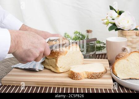 un panettiere taglia una fetta di un filone intrecciato di pane all'uovo di sesamo su un tagliere di legno Foto Stock