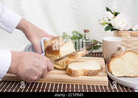 un panettiere taglia una fetta di un filone intrecciato di pane all'uovo di sesamo su un tagliere di legno Foto Stock