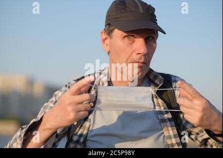 L'uomo caucasico in abbigliamento casual tiene una maschera medica all'aperto Foto Stock