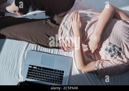 Procrastinazione, riposo dal lavoro: Una donna si appoggia a letto accanto ad un computer. Concetto di lavoro remoto, non essere in grado di essere produttivo, essere pigro lavoro Foto Stock