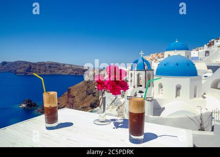 Drink rinfrescante e fiori su un tavolo di legno sullo sfondo dell'isola di Santorini Foto Stock
