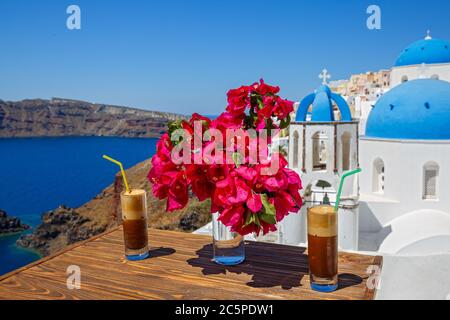 Drink rinfrescante e fiori su un tavolo di legno sullo sfondo dell'isola di Santorini Foto Stock