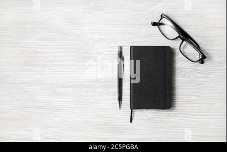Blocco note nero, bicchieri e matita su sfondo tavolo in legno chiaro. Spazio per copiare il testo. Disposizione piatta. Foto Stock