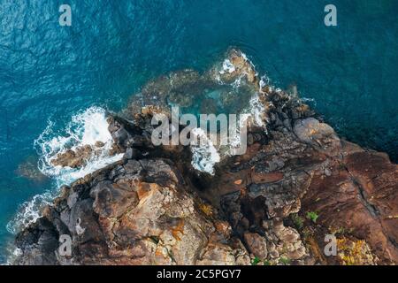 Vista aerea dall'alto delle onde turchesi dell'oceano Atlantico che si infrangono sulle rocce sulla riva portoghese dell'isola di Madera. Foto Stock