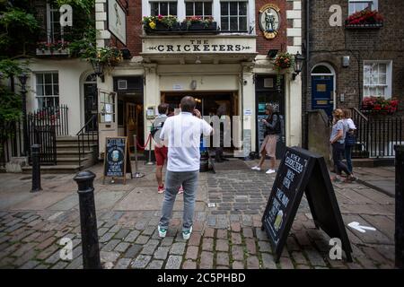 Code fuori dalla casa pubblica "The Cricketers" durante la graduale riapertura dopo il blocco del Coronavirus COVID-19, The Green, Richmond, Southwest London Foto Stock