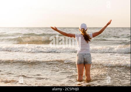 Ragazza in una T-shirt bianca e cappuccio si erge contro il mare Foto Stock