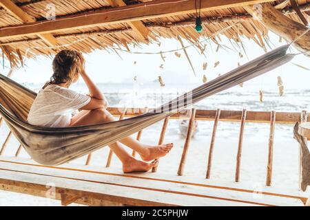 Giovane donna seduta in amaca sulla terrazza della capanna di paglia e godendo di un paesaggio di spiaggia sul mare sulla spiaggia di Tonsai in Thailandia. infaticabile estate esotica va Foto Stock