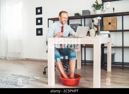 Situazione comica moderna dell'ufficio domestico. Uomo d'affari ha una  videochiamata che chattava sul computer portatile e che si alza in piedi  caldo bagno sotto il tavolo. Lavoro a distanza Foto stock 