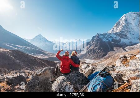 Giovane coppia che gioisce sulla rotta di trekking Everest base Camp vicino Dughla 4620m. Backpackers sinistra zaini e bastoni da trekking e godendo vista valle w Foto Stock