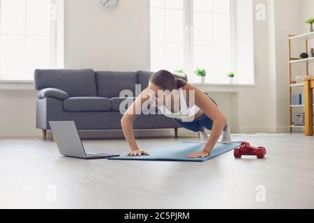 Bella fit ragazza in sportswear guardando video di allenamento online e. fare spingere su o fare esercizio a livello a casa Foto Stock