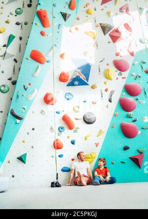 Padre e figlio adolescente seduto vicino alla parete interna di arrampicata. Riposano dopo l'arrampicata attiva. Felice immagine concettuale parenting. Foto Stock