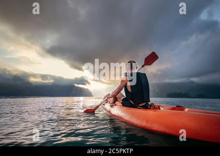 Uomo che galleggia in kayak al mattino sotto il cielo dell'alba sul lago Cheow LAN, Khao Sok National Park, Thailandia Foto Stock