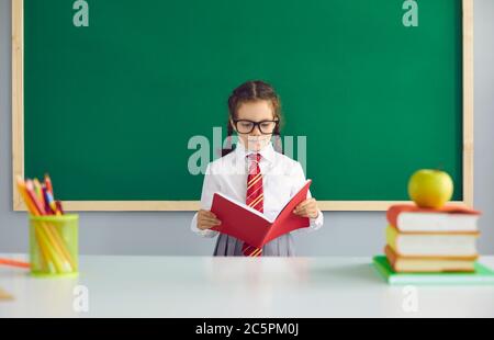 Ritorno a scuola. Una studentessa impegnata legge un grande libro mentre si trova alla lavagna della scuola in classe. Foto Stock