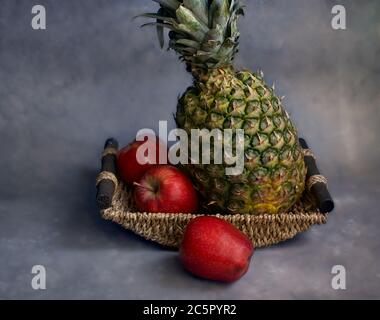 Ananas in un cestino con tre mele rosse Foto Stock