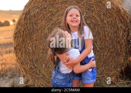 Girlfriends coccolarsi vicino ad un haystack in un campo in estate Foto Stock