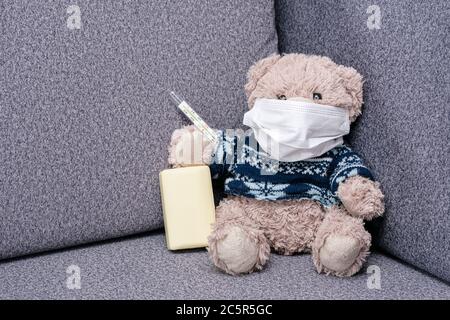 L'orso si siede sul divano in maschera medica protettiva. Maschera protettiva per la protezione contro il coronvirus e l'epidemia di influenza. Aiuto visivo per i bambini circa i mezzi di Foto Stock